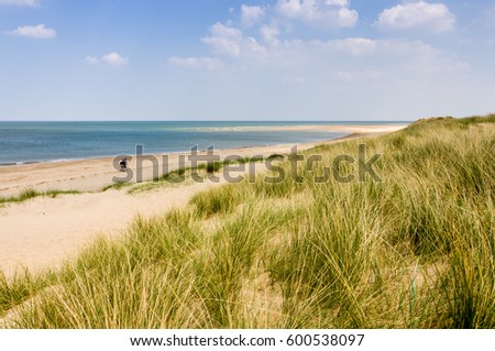 Two people with rucksacks walking down a sandy beach on a sunny day in Burnham Overy Staithe, Norfolk, England, UK.