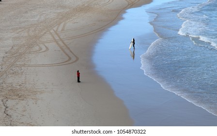 Two People At The Same Beach In Different Situation, One On Cold, One On Surf