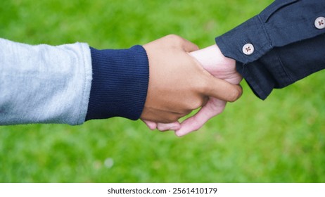 Two people shaking hands in a grassy field. Scene is friendly and welcoming