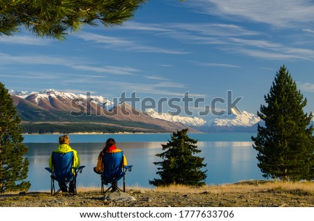 Two people sitting on camping chairs looking at distant Mount Cook across Lake Pukaki, South Island, New Zealand