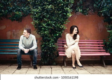 Two People Sitting On Different Benches Looking To Opposite Sides