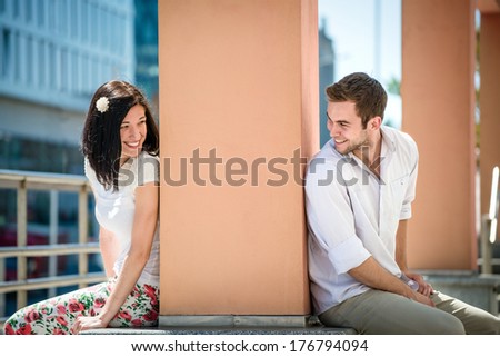 Two people sitting on opposite side of big collumn - outdoor in street