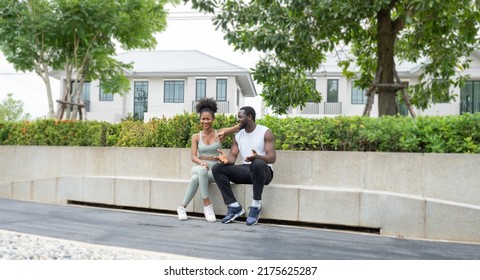 Two People Sitting In The Park Have Fun Talking After Morning Jogging. Cheerful Young Couple Enjoy Leisure Outdoor In A Green Garden. Husband And Wife Happy Healthy Together Concept. 