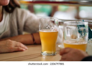 Two People Sitting At A Table With Two Glasses Of Beer.