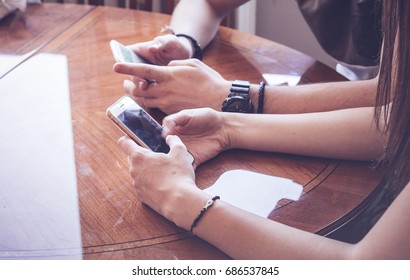 Two people sitting and using their smart phones next to each other