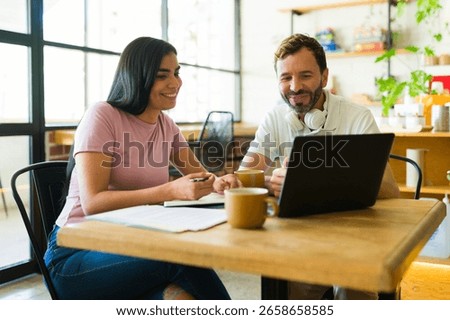 Two people smiling and collaborating on a project using a laptop in a coffee shop, enjoying coffee and remote work