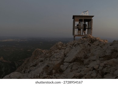 Two people standing inside a mountain observation cabin while enjoying the early morning light.