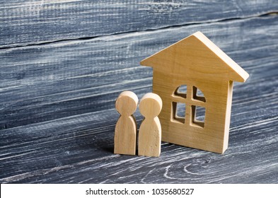Two people are standing near the house. Wooden figures of persons stand near a wooden house. The concept of a couple in love, cohabitants, parents, buyers and sellers at home. They live in the house. 