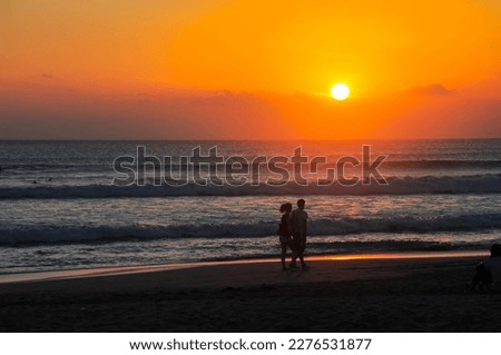 two people standing on the beach watching the sun go down . 