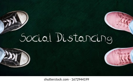 Two People Standing On Chalkboard With The Word Social Distancing In Between. Concept Of Staying Physically Apart For Infection Control Intended To Stop Or Slow Down The Spread Of COVID-19 Conoravirus