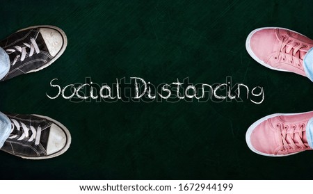 Two people standing on chalkboard with the word social distancing in between. Concept of staying physically apart for infection control intended to stop or slow down the spread of COVID-19 conoravirus