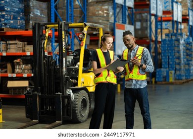 Two people are standing in a warehouse, one of them is holding a clipboard. The warehouse is filled with boxes and crates, and there is a forklift in the background. Scene is serious and focused - Powered by Shutterstock