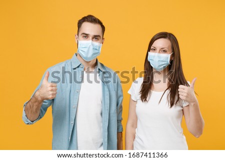 Two people in sterile face masks white t-shirts isolated on yellow background studio. Epidemic pandemic rapidly spreading coronavirus 2019-ncov medicine flu virus ill sick disease treatment concept