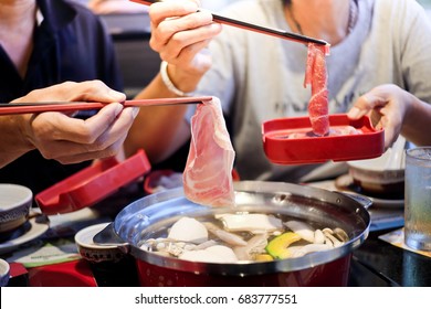 Two people are taking meat and pork slides into a hot pot