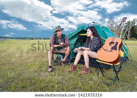 Two people talking near camping tent in meadow field. Male and female traveler looking at attraction view point. Couples adventure at outdoors together. People and lifestyles concept