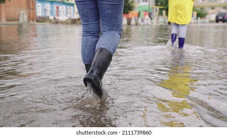 Two People Walk Through Puddles Of Flooded City Rubber Boots On Their Feet, Teamwork, Girls Summer Raincoats, Lot Of Rainwater Is Poured On Street, Natural Weather Phenomena, Walking Boots On Road