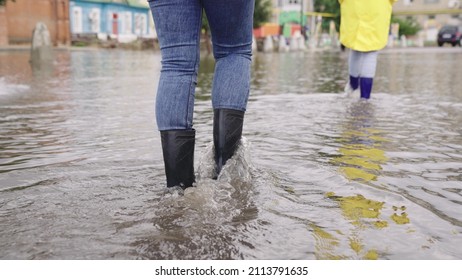 two people walk through puddles of flooded city rubber boots on their feet, teamwork, girls summer raincoats, lot of rainwater is poured on street, natural weather phenomena, walking boots on road