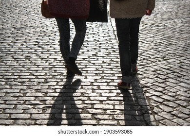 Two People Walking Down The Street With Stone Floor And Its Shadows