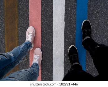 Two People Walking On Colored Stripes On The Asphalt Of The Street, A Woman In Pink Shoes And A Man In Black Shoes