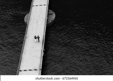 Two People Walking On A Floating Bridge Near The Port Of Geiranger In Norway.