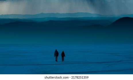 The Two People Walking Through The Snow Field On The Night Sky Background