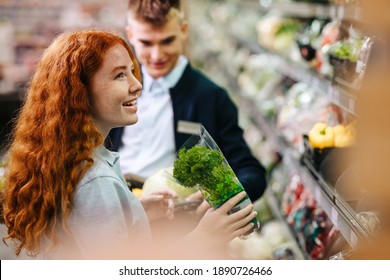 Two People Working In The Produce Section Of A Supermarket. Man And Woman Supermarket Trainee Employees At Work Holding Fresh Vegetables While Stocking Up The Aisles.