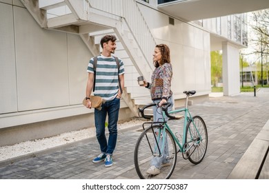 Two people young adult couple man and woman boyfriend and girlfriend or students friends walk by the building or university in day with bicycle and skateboard modern lifestyle concept copy pace - Shutterstock ID 2207750387