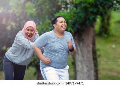 Two People, With Young Muslim Women Encouraging Asian Male Friends Who Are Overweight To Exercise That Is Running In An Outdoor City Park