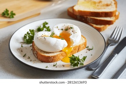 Two perfectly poached eggs, one with a runny yolk, are served on toasted bread slices on a white plate, garnished with fresh herbs and pepper, next to cutlery on a light textured surface.