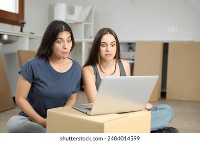 Two perplexed roommates checking laptop while moving house