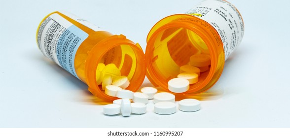Two perscription bottles with pain pills spilling out of them with a white background. 