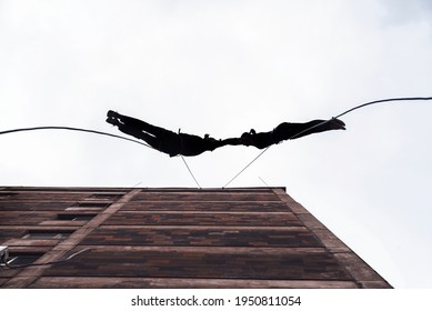 Two Person Silhouettes, Dancing In The Air, Tied By The Ropes On The Roof. Extreme Rope Dance On The Wall Of A Tall Building. 