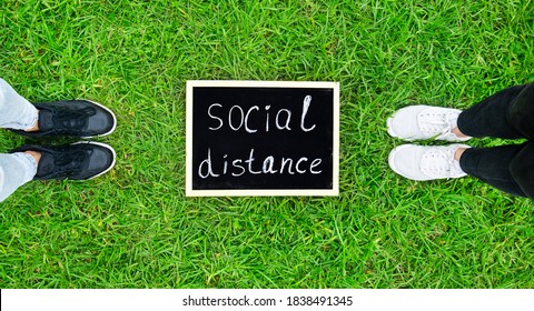 Two Person Stay Away Each Other Keeping Social Distance On The Grass In Park. Concept Of Staying Physically Apart For Infection Control Intended To Stop Or Slow Down The Spread Of COVID-19 Conoravirus