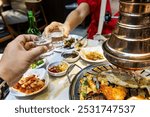 Two person toasting soju drinks during dinner in Korean barbecue restaurant while enjoying grilled meats.