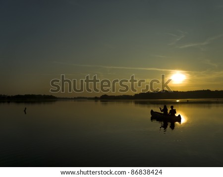 two persons sitting in a boat and facing dawn