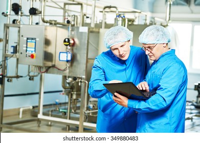 Two pharmaceutical technician male workers in water preparation production line hall at pharmacy industry manufacture factory using notebook computer