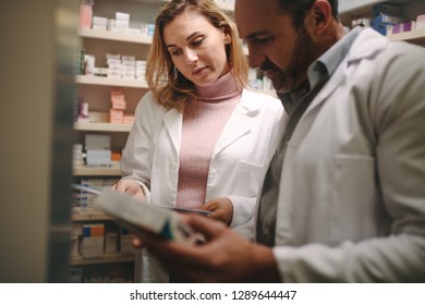 Two Pharmacist Holding Prescription And Checking Medicine In Pharmacy Store. Man And Woman Pharmacists Searching For A Medication In The Storage Of The Pharmacy Store.