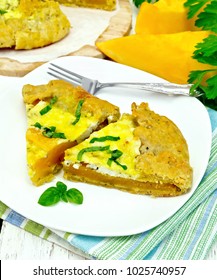 Two piece of the pie of pumpkin, salty feta cheese, eggs, cream and herbs in a plate on a napkin, parsley and basil on the background light wooden boards