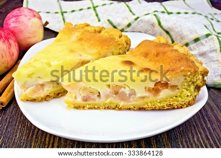Two pieces of apple pie with cream sauce in white plate, cinnamon, napkin on dark wooden board