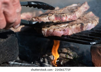 Two Pieces Of Beef On A Barbecue With Small Flame. Wood Fire Grill. Making Dinner Outdoor. Summer Picknick Close Up. 