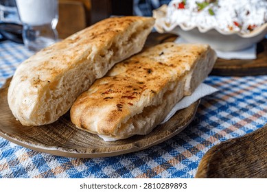 Two pieces of cooked bread rest on a wooden plate in a busy cafe. People eat nearby and enjoy their meals.