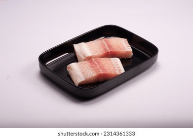 Two pieces of fresh dory fish arranged in black plastic tray, isolated on white background