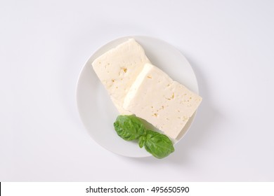 Two Pieces Of Fresh Feta Cheese With Basil On White Plate