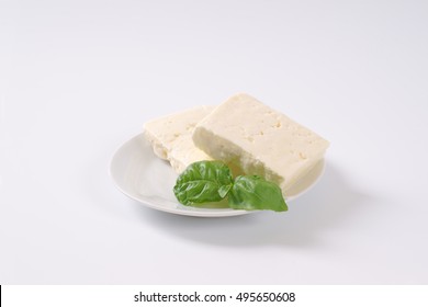 Two Pieces Of Fresh Feta Cheese With Basil On White Plate