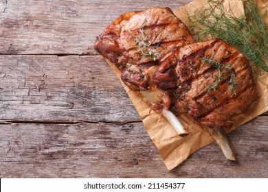 two pieces of of grilled pork with herbs on a paper on an old table top view horizontal close-up  