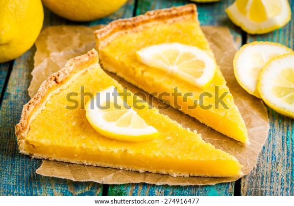 two pieces of lemon tart with slice of lemons\
closeup on rustic blue\
table
