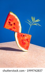 Two pieces of watermelon with a palm leaf balancing on a blue background. Concept of summer, freshness and balance