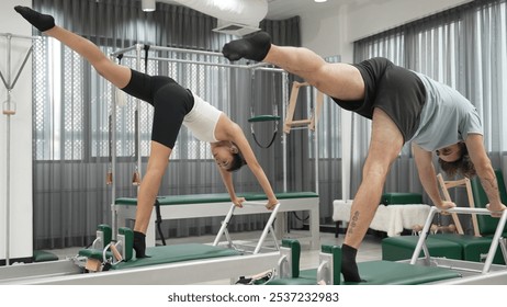 Two Pilates client performing synchronized handstand variations on reformer machines. Group of pilates partner doing downward dog split on the reformer for strengthen arm and core. Balance. Habituate. - Powered by Shutterstock