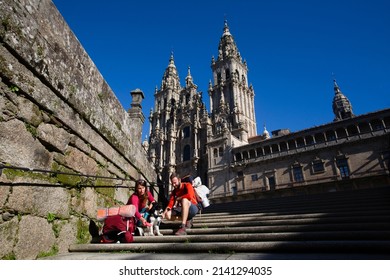 Two pilgrims finish the Camino de Santiago and rest on the steps of Plaza del Obradoiro in front of the Cathedral of Santiago de Compostela