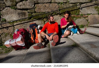 Two pilgrims finish the Camino de Santiago and rest on the steps of Plaza del Obradoiro in front of the Cathedral of Santiago de Compostela